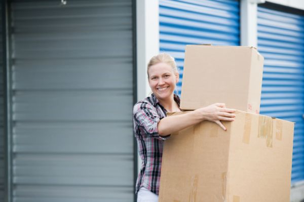 person holding moving boxes in front of an open self storage unit
